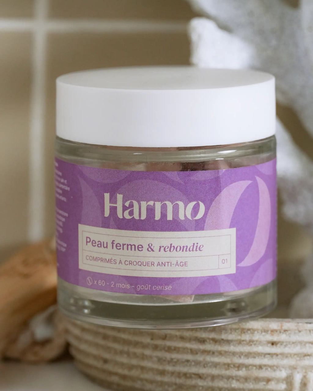 Pot de comprimés à croquer Harmo Anti-âge Peau ferme et rebondie posé dans une salle de bain moderne, mise en scène quotidienne du produit