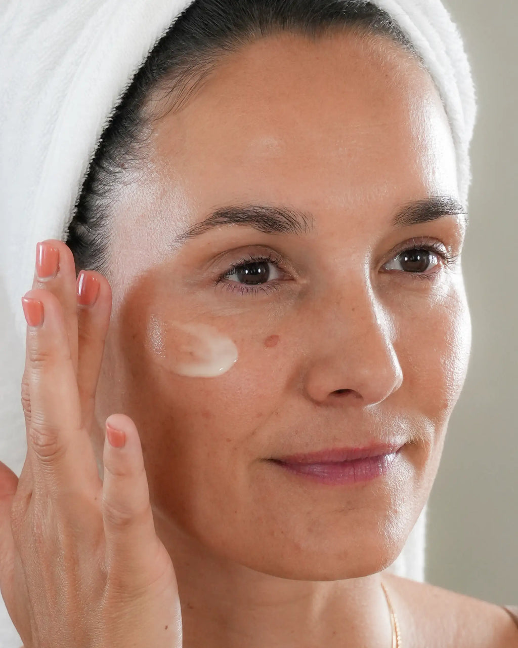 Femme avec serviette sur la tête qui applique le sérum Anti-âge Harmo Peau ferme et rebondie sur la joue, texture blanche