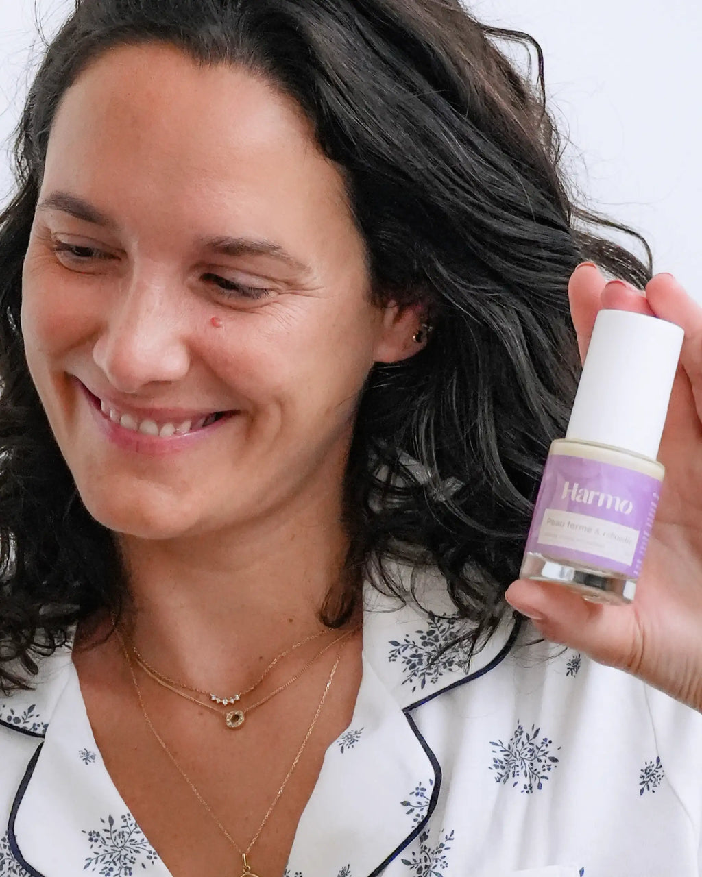 Femme tenant le sérum Anti-âge Harmo Peau ferme et rebondie dans sa main, sourire